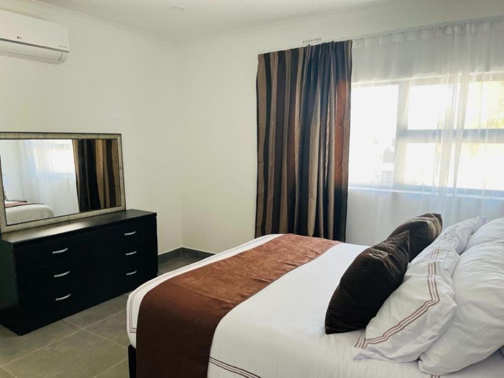 een slaapkamer met een bed met een spiegel en een dressoir bij Comfy Zone Apartment in Gaborone