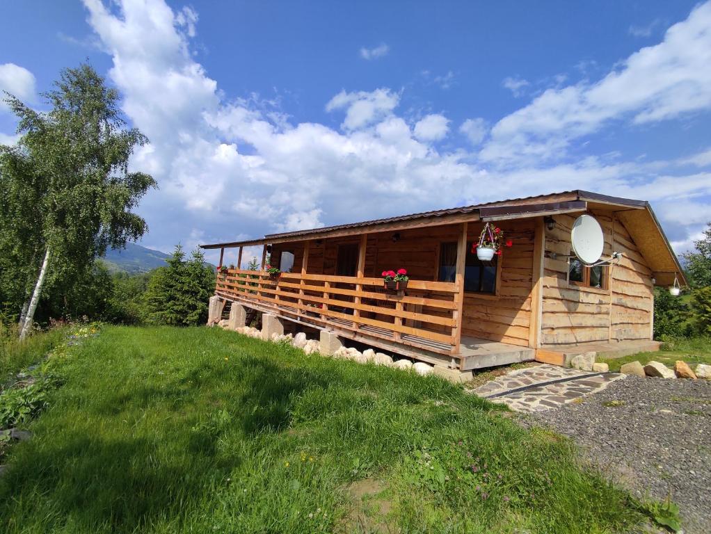 a wooden cabin with a porch on a grass field at Cabana doi mesteceni in Drumu Carului