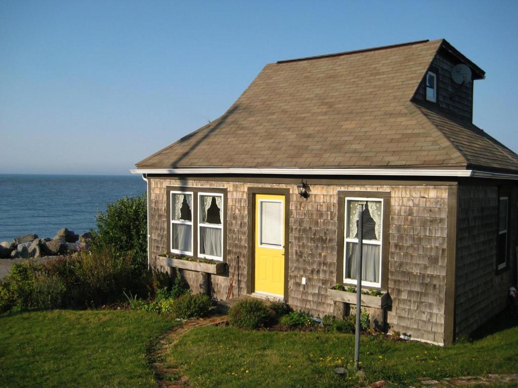 una pequeña casa con una puerta amarilla y el océano en Little Bird Inn, en Margaretsville
