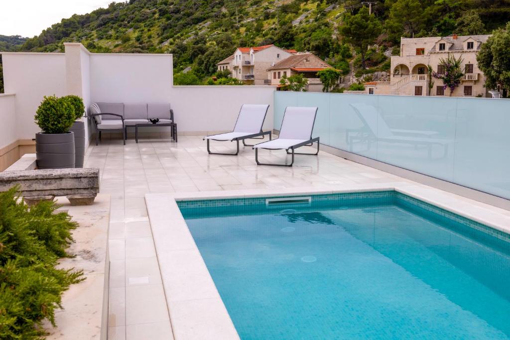 a swimming pool with two chairs next to a white wall at Insula Apartment with Private Pool in Pučišća