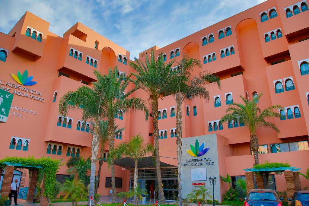 an orange building with palm trees in front of it at Labranda Rose Aqua Parc in Marrakech