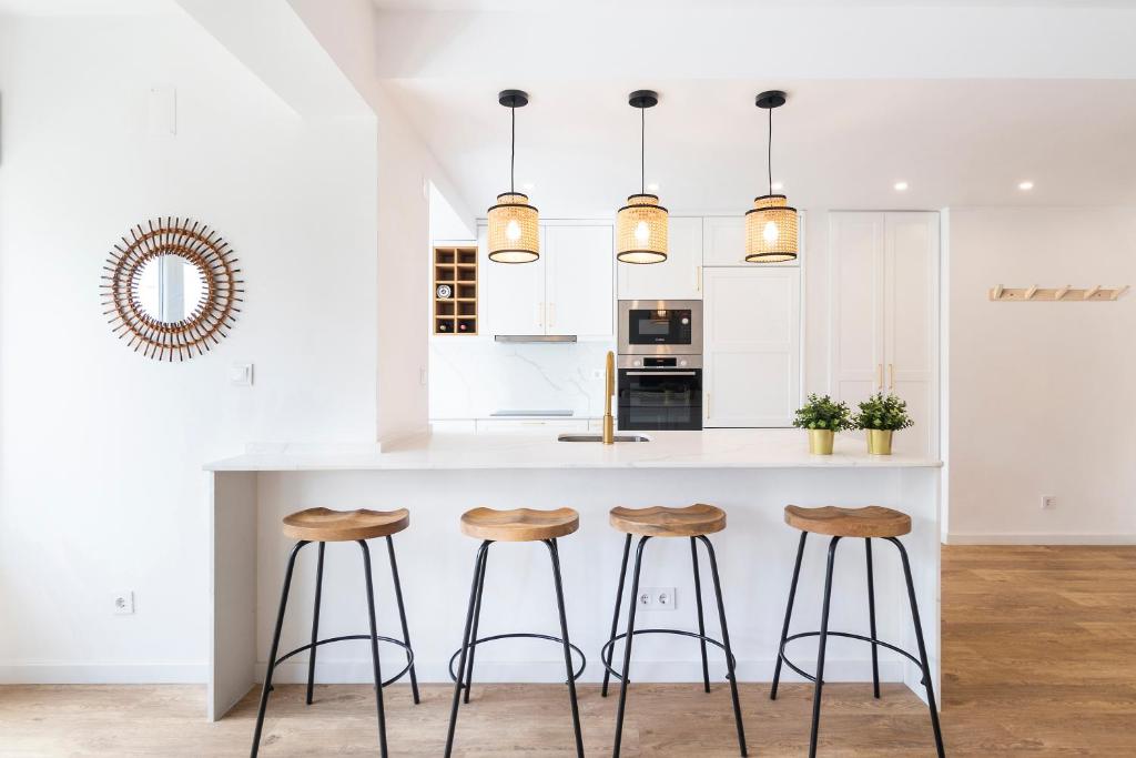 Oeiras Apartment في أويراس: مطبخ مع دواليب بيضاء وكاونتر مع الكراسي