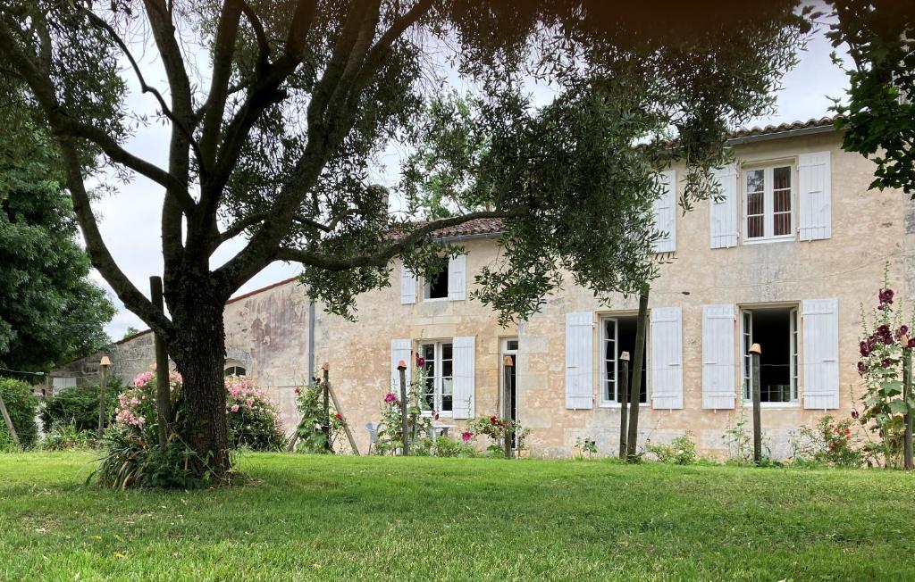 une grande maison en pierre avec un arbre dans la cour dans l'établissement Gite des Noisettes à la porte de Saintes, à Chermignac