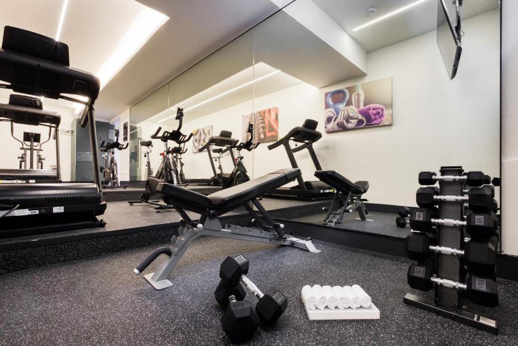 A mirrored fitness room with treadmills, bikes, a bench and free weights.