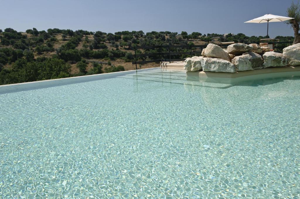 uma grande piscina com água azul e um guarda-sol em Relais Parco Cavalonga em Donnafugata