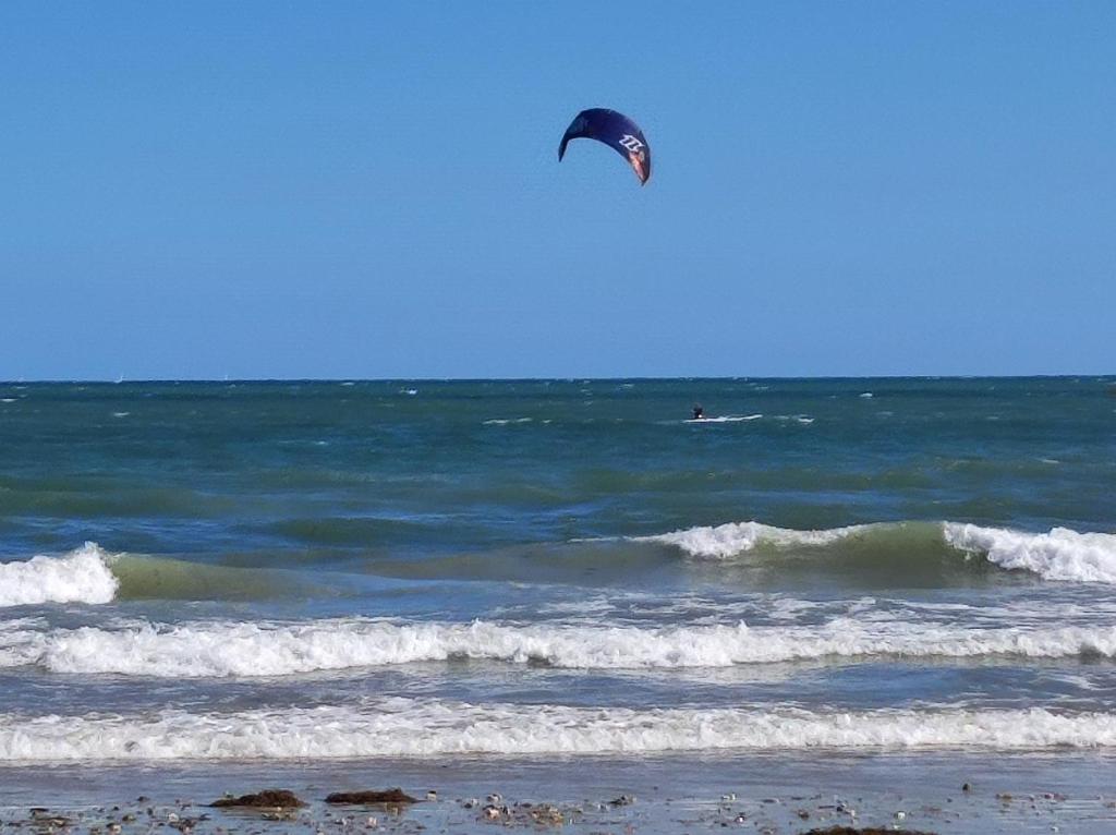a person flying a kite over the ocean at Sur le chemin de la plage in Cherbourg en Cotentin