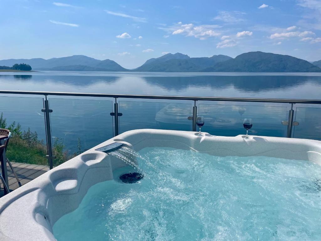 uma banheira de hidromassagem com vista para a água em Loch Linnhe Waterfront Lodges with Hot Tubs em Glencoe