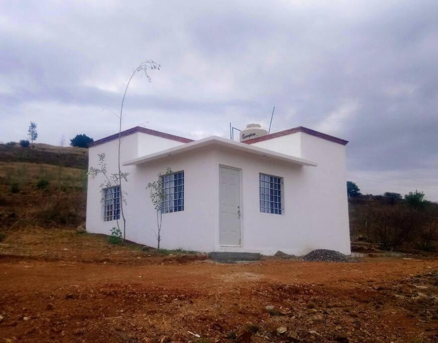una pequeña casa blanca en medio de un campo en Bungalow en la mejor ruta turística de Oaxaca, en San Jerónimo Tlacochahuaya