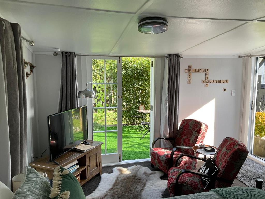 sala de estar con 2 sillas y TV en Orange Tree Cottage - garden hideaway en Whanganui