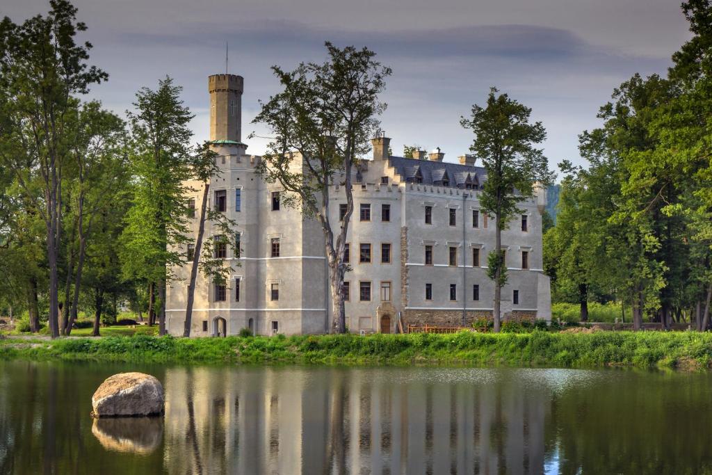 White historic castle beside a reflective pond with trees and solitary rock, peaceful overcast light.