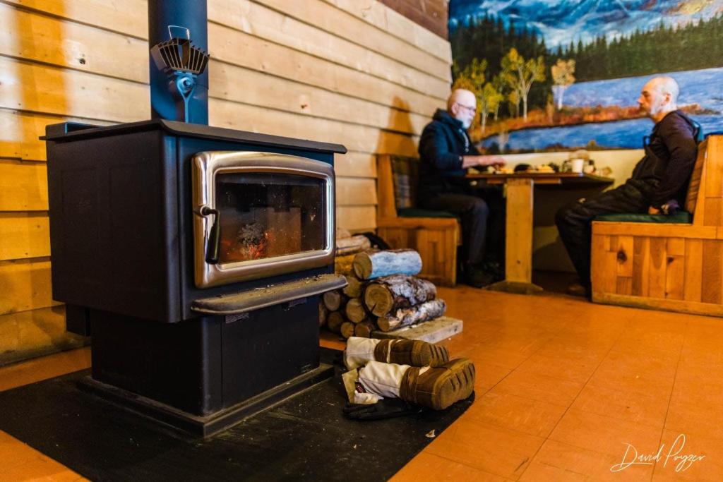 una estufa de leña en una habitación con dos hombres en McGrath Roadhouse, en McGrath