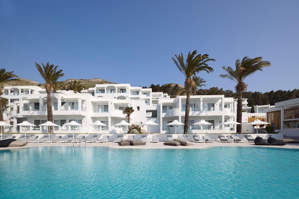 a large white building with palm trees and a swimming pool at Dimitra Beach Hotel & Suites in Agios Fokas