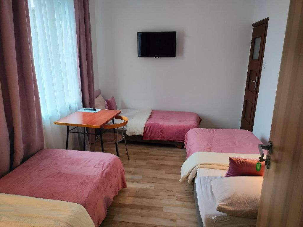 a room with three beds and a table and a television at Hostel 11 in Kozienice