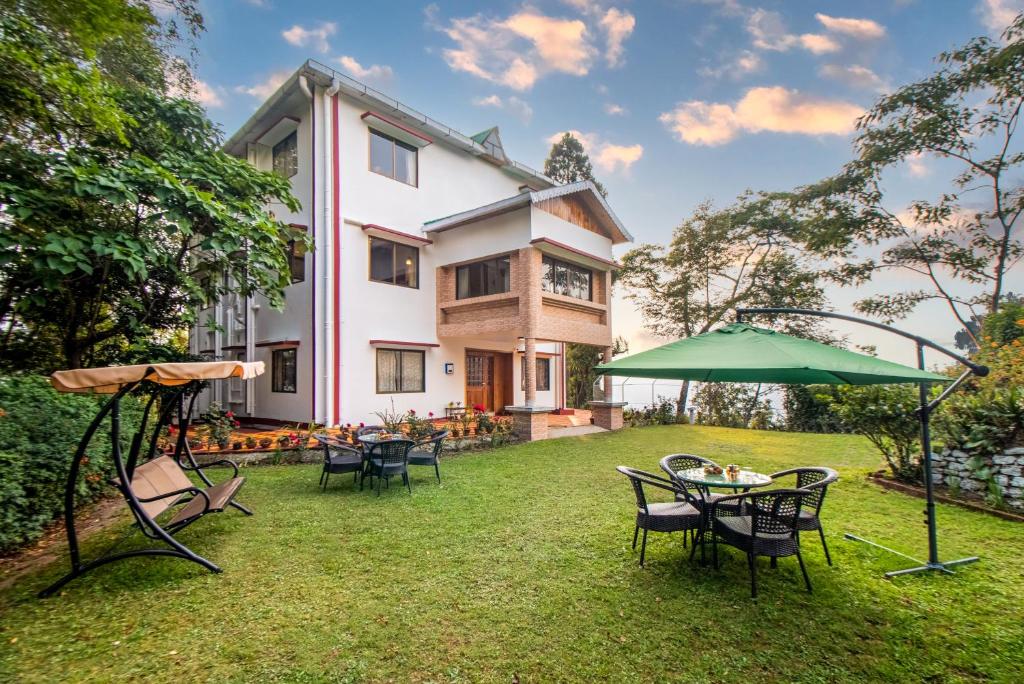 a patio with chairs and an umbrella in front of a house at StayVista's Tree Tops & Tea Trails - Mountain-View Villa Amidst Tea Plantation with Telescope & Gazebo in Darjeeling