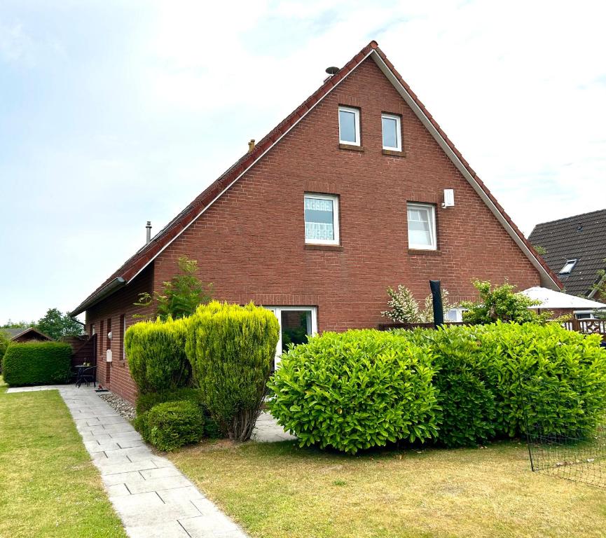 a red brick house with bushes in front of it at FeWo Lüttje Wooge Dornum in Dornum