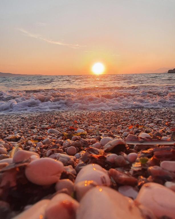 a pebble beach with the sun setting over the ocean at Mihal Suites in Sarandë