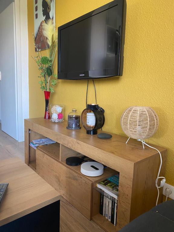 a tv on a yellow wall with a wooden entertainment center at Appartement T2 Lège Cap Ferret in Lège-Cap-Ferret