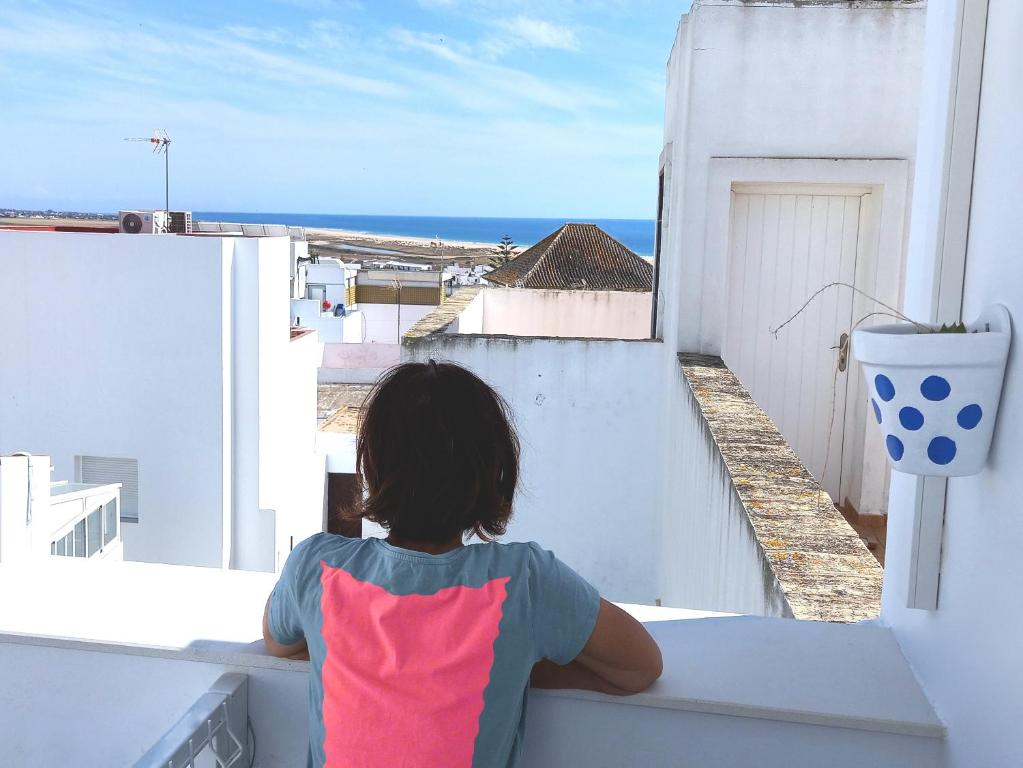 a woman sitting on a balcony looking out at the ocean at Casa Malakita with private seaview roof terrace in Conil de la Frontera