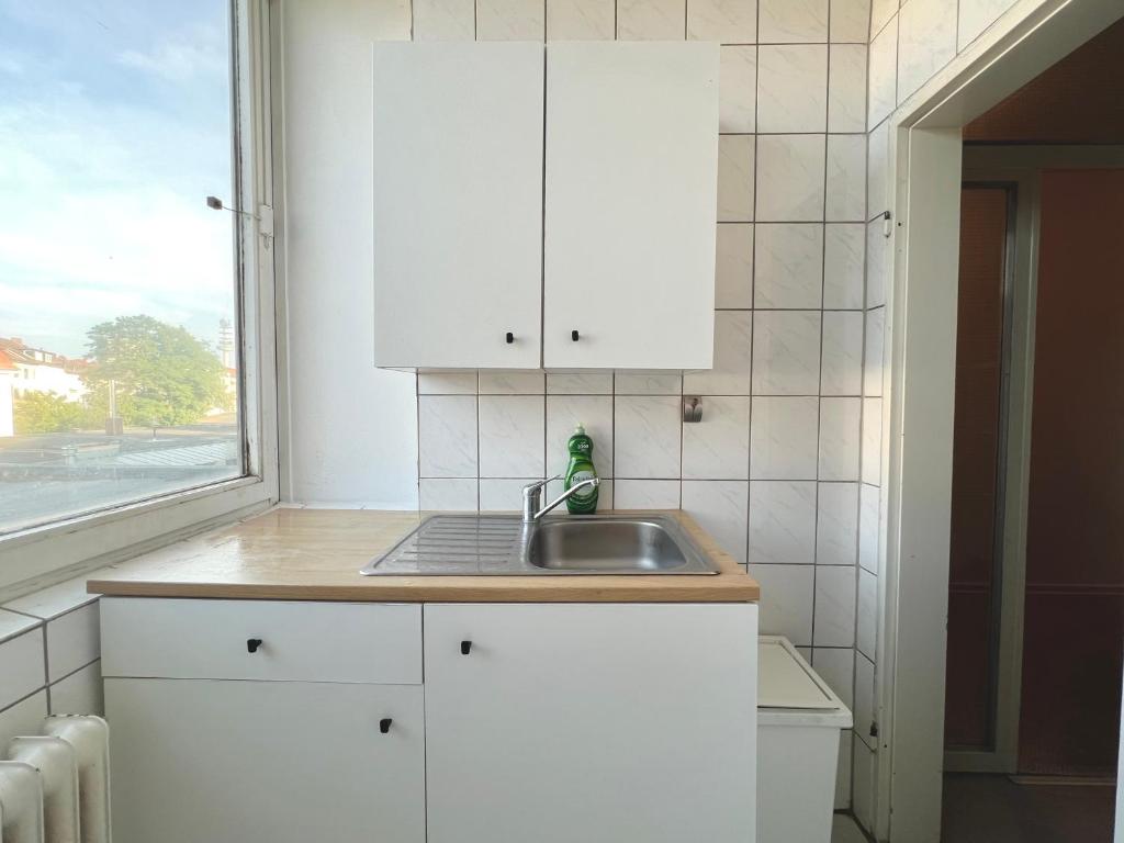 uma cozinha com armários brancos, um lavatório e uma janela em Monteurwohnung in Stadtnähe em Hanôver