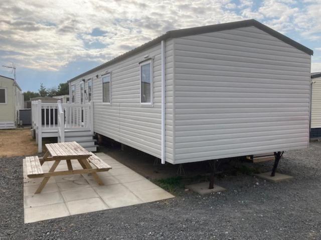 a white tiny house with a picnic table and a bench at 3 Bedroom Modern Caravan Sleeps up to 8 in Millom