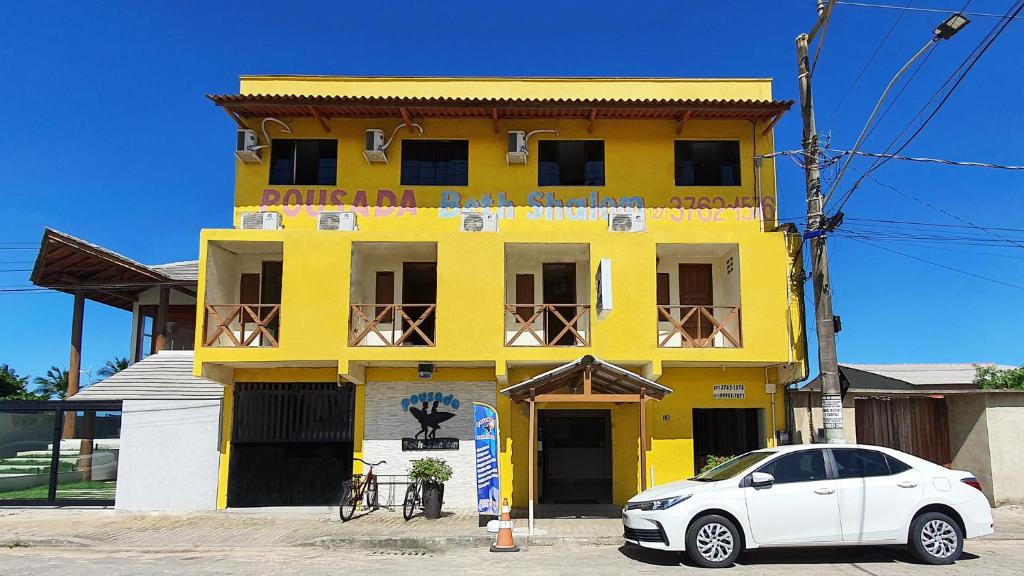 un coche blanco estacionado frente a un edificio amarillo en Pousada Beth Shalom en Conceição da Barra