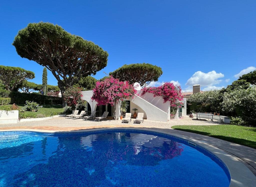 a swimming pool in front of a house with pink flowers at Traditional 3 bedroom villa with great pool in the heart of Vale do Lobo in Vale do Lobo