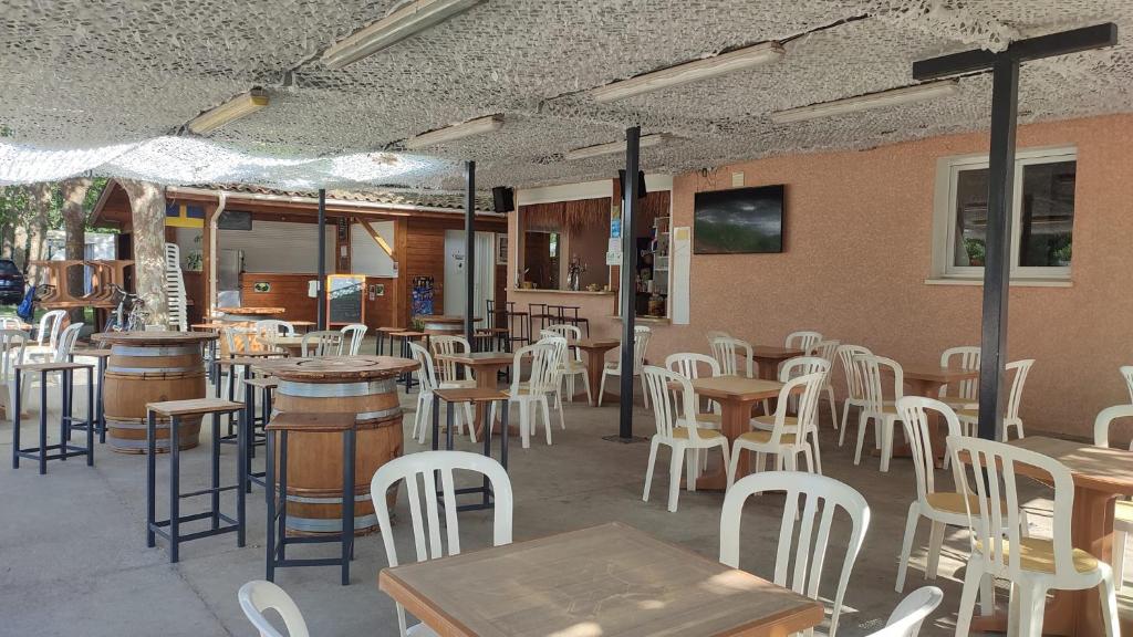 a restaurant with tables and white chairs and tables andools at CAMPING LE NAVARRE *** in Vias