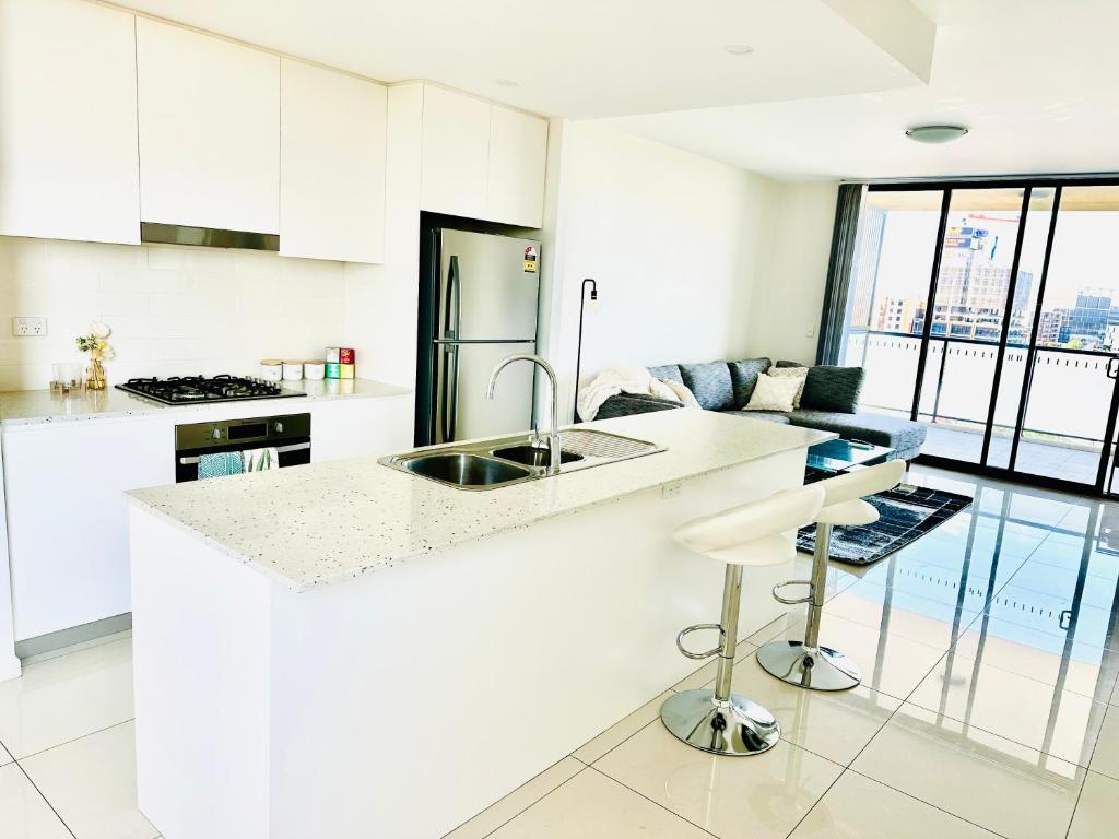 a white kitchen with a sink and a counter at Modern 2 bedroom & 2 bathroom apartment with stunning Sydney CBD & Skyline Views! in Liverpool