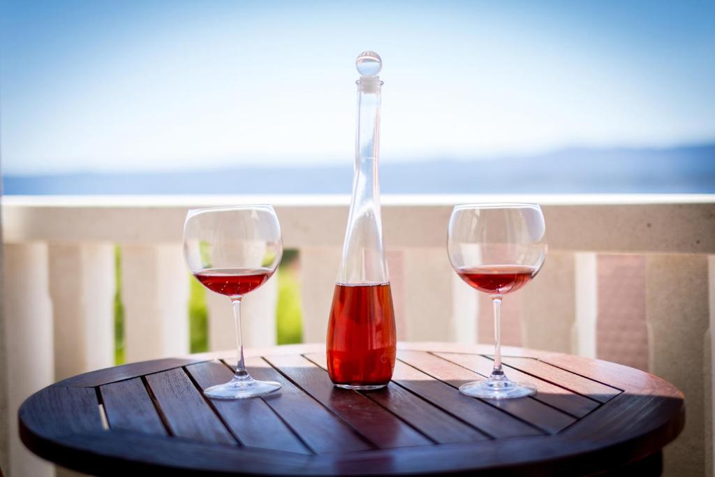 dos copas de vino en una mesa con una botella en Zlatni Bol Apartments en Bol