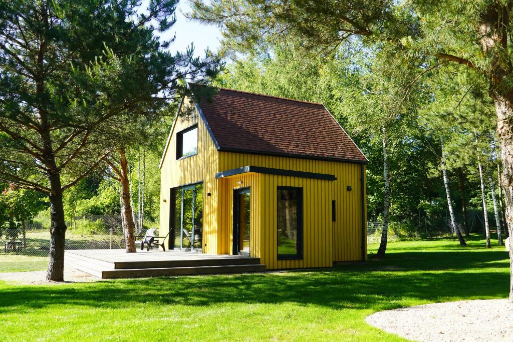 une petite maison jaune dans un parc arboré dans l'établissement Wioska Radoska - Żółta Stodoła, à Lichtenstein Ostpreussen