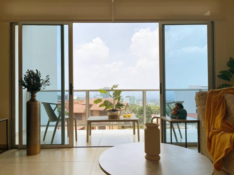 Una sala de estar con una gran ventana de vidrio con una persona sentada en una mesa. en Encanto Urbano, en San Salvador