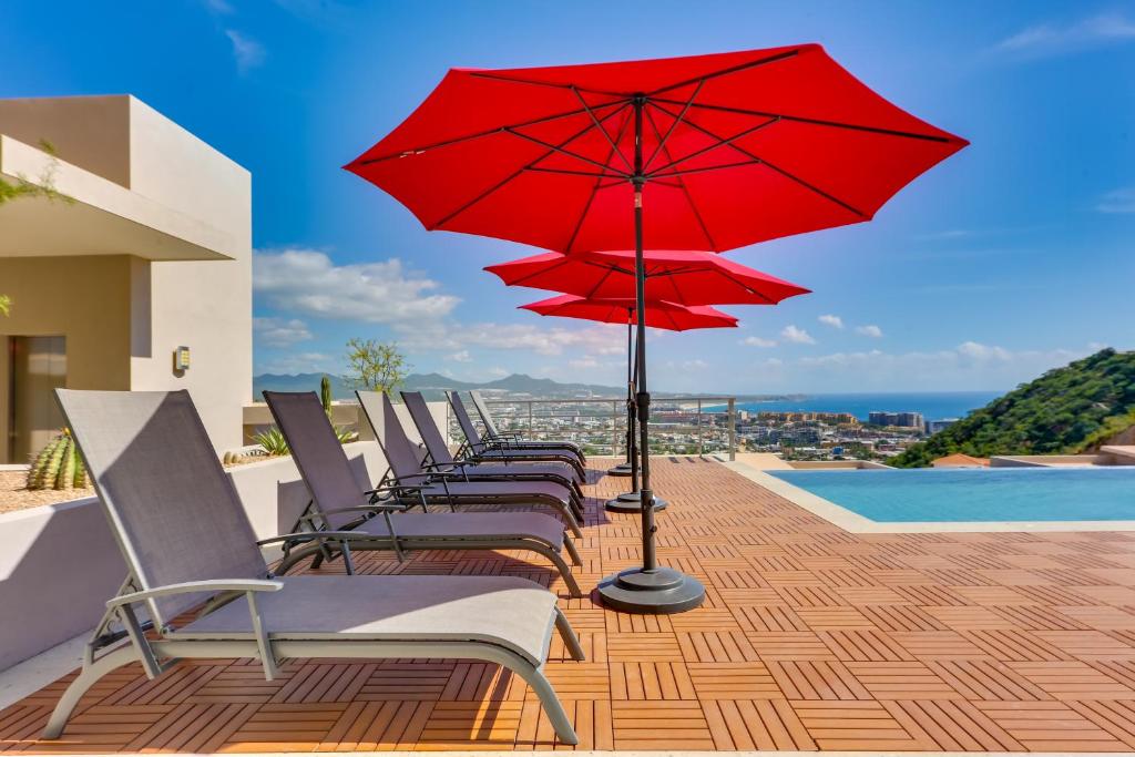eine Reihe von Stühlen mit roten Sonnenschirmen auf einem Balkon in der Unterkunft Cabo Pedregal Condo Ocean View and 2 Infinity Pools in Cabo San Lucas