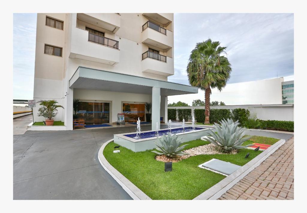 un grand bâtiment blanc avec un palmier en face dans l'établissement MG Flats Hotel & Residence, à Cuiabá