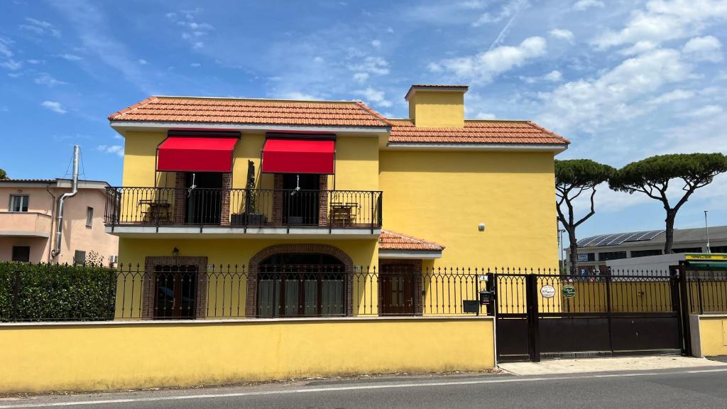 a yellow house with red awnings and a black fence at Guest House Le Vagabonde in Fiumicino