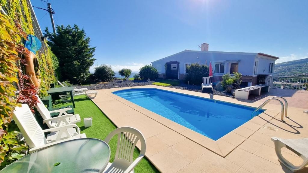 a swimming pool with chairs and a house at Loreto Rose, Panoramic Ocean and Mountain View in Arco da Calheta