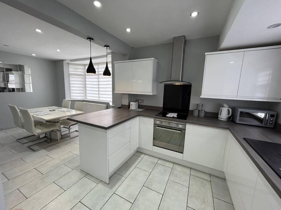 a kitchen with white cabinets and a table in it at Fresh & Spacious House in Rhyl