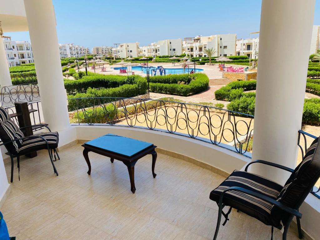 balcón con sillas, mesa y piscina en شالية Golden Beach 1, en Raʼs Matarma
