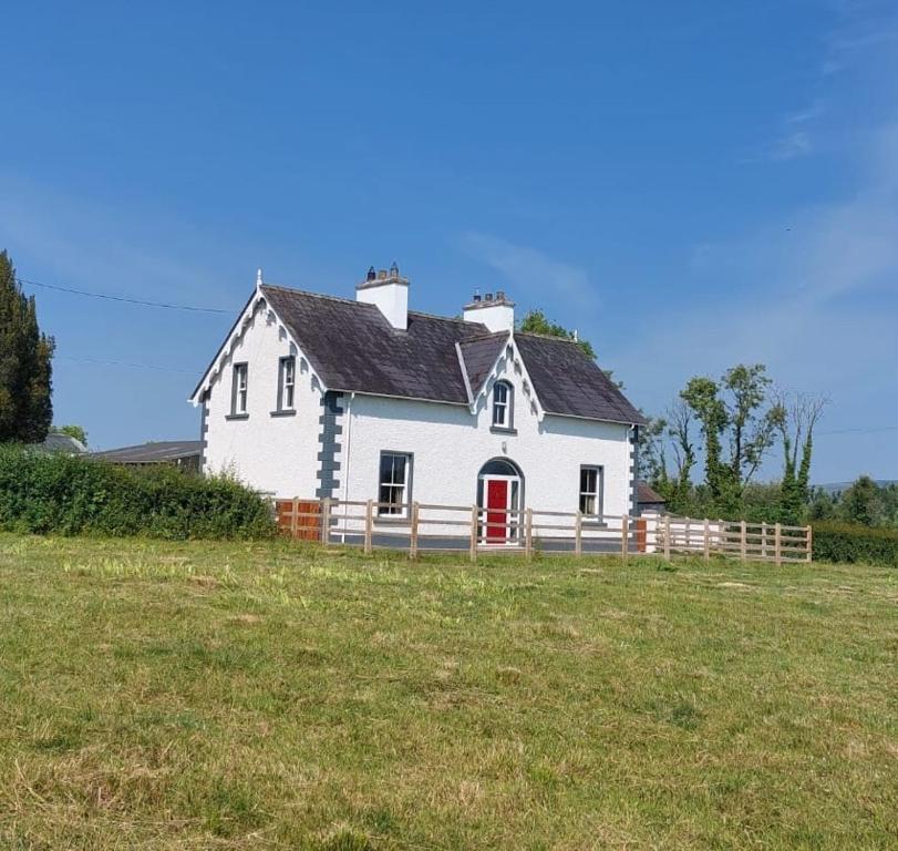 una casa blanca con una puerta roja en un campo en Drumlaghy House, en Florencecourt