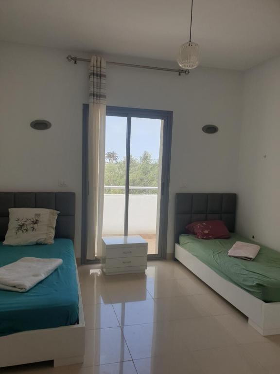 2 camas en una habitación blanca con ventana en Villa Château D'eau Djerba, en Awlād ‘Umar
