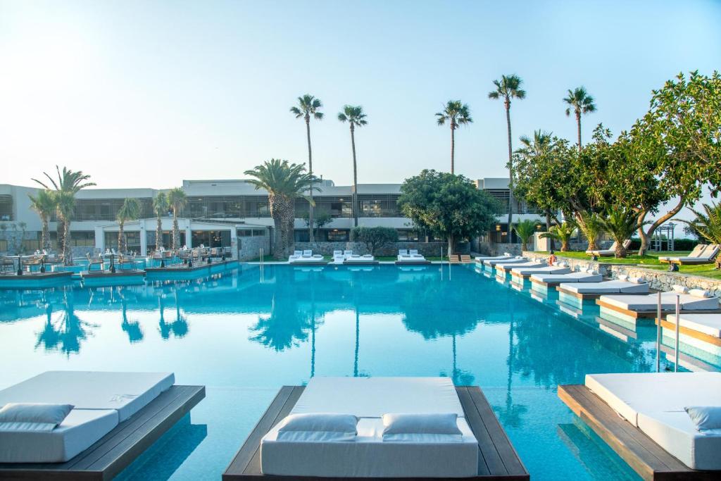 a large swimming pool with lounge chairs and palm trees at KING MINOS RETREAT Resort & Spa in Hersonissos