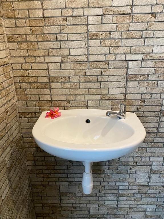 a white sink with a red flower on a brick wall at New Anugrah Hotel in Teluk Nara