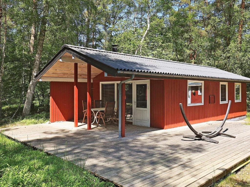 eine rote Hütte mit einer Holzterrasse im Wald in der Unterkunft Holiday home Stege XVII in Stege