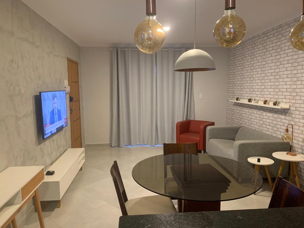 ein Wohnzimmer mit einem Tisch, einem Sofa und einem TV in der Unterkunft Apto térreo novo 3 dorm - próximo ao centro in Poços de Caldas