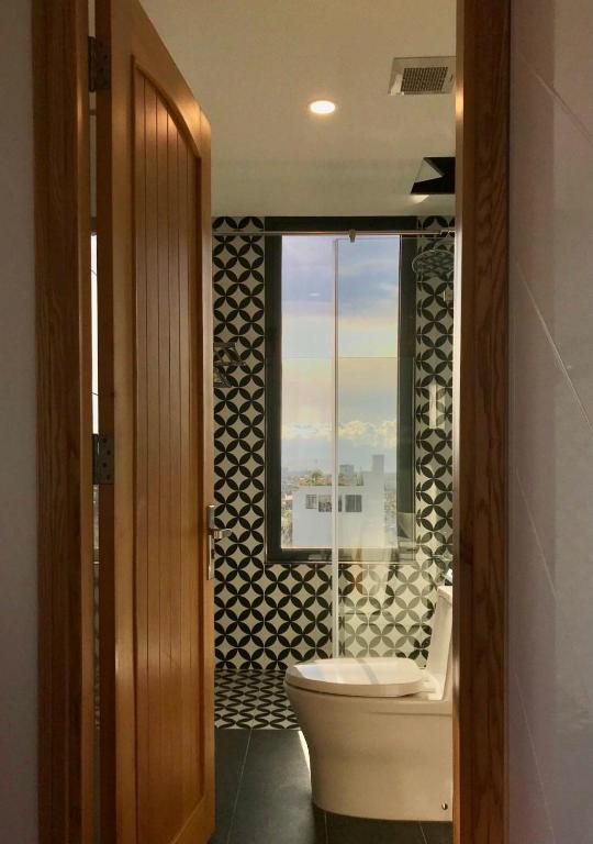 A narrow bathroom entrance framing a toilet, patterned tile and a window view.