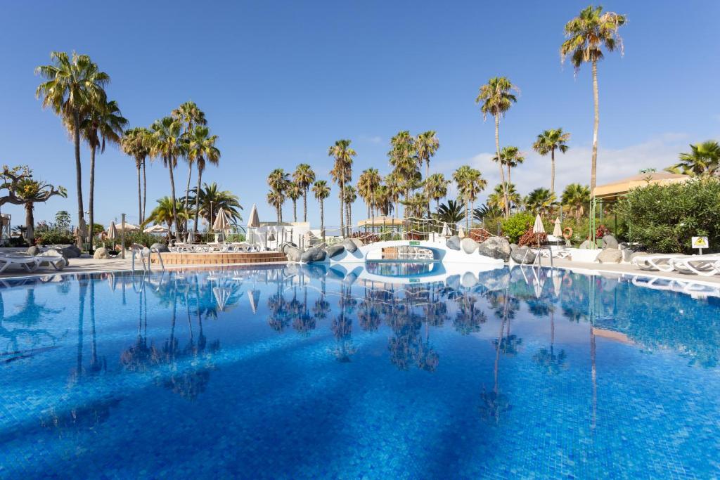 uma grande piscina com palmeiras ao fundo em 220 TROPICAL DUQUE Paradise by Sunkeyrents em Adeje
