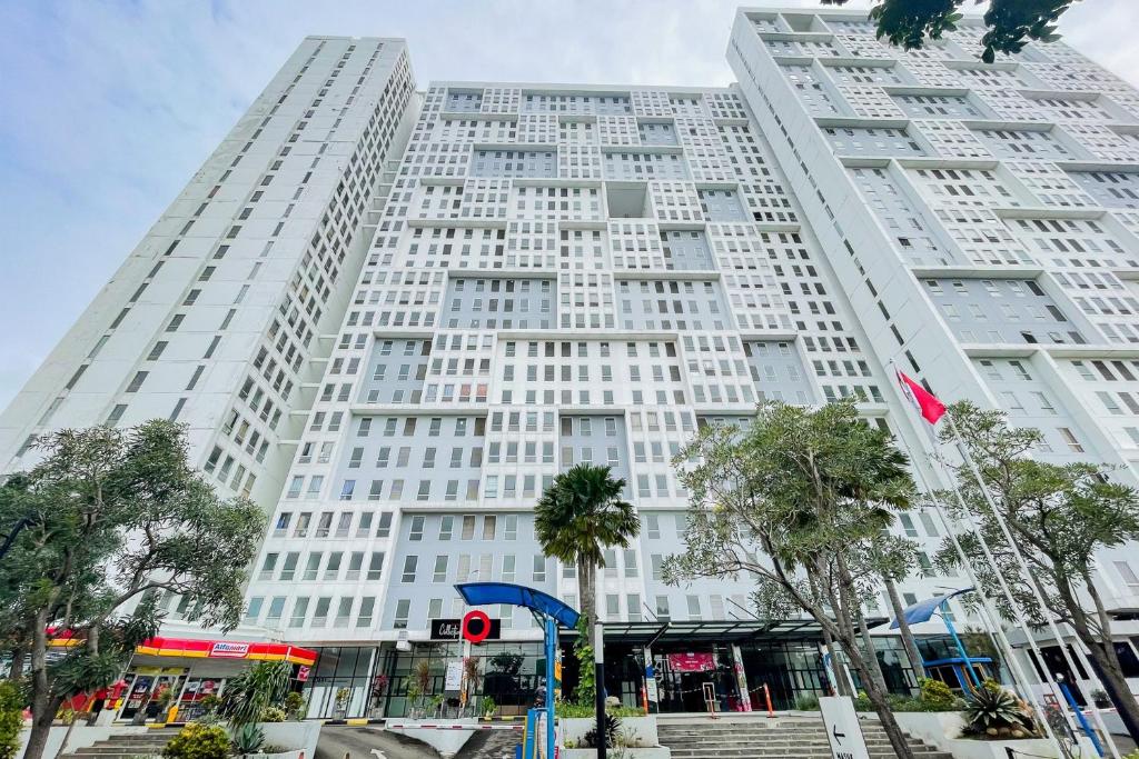 ein großes weißes Gebäude mit Bäumen davor in der Unterkunft RedLiving Apartemen Patra Land Urbano - Happy Rooms Tower Mid-West with Netflix in Bekasi