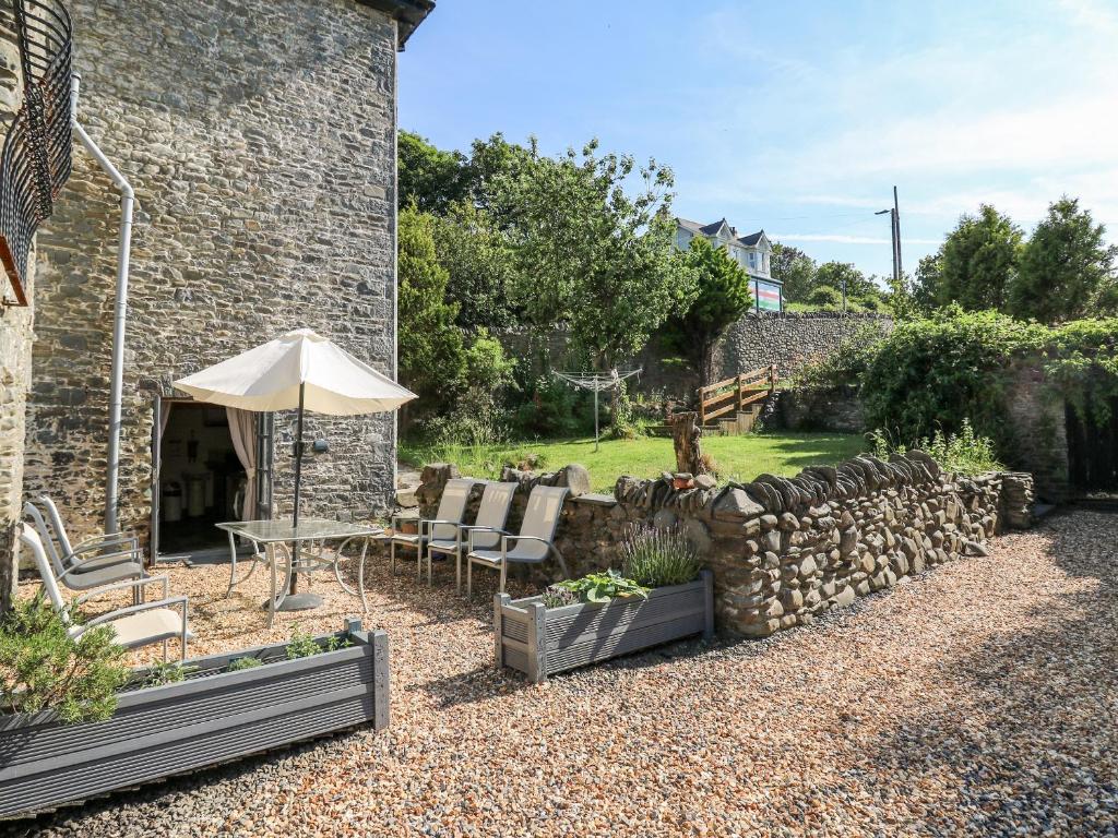 a patio with an umbrella and chairs and a stone wall at Dewi Villa in Aberaeron