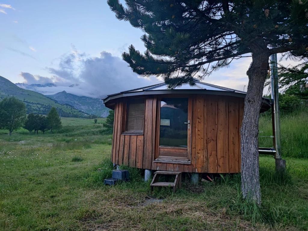 een houten hut naast een boom in een veld bij Auberge du Col du Festre in Le Dévoluy