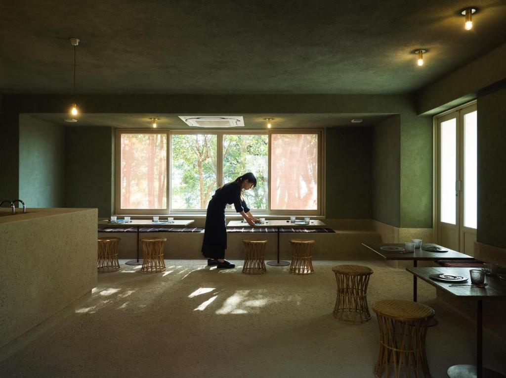 a woman standing in a room with tables and chairs at LOG in Onomichi