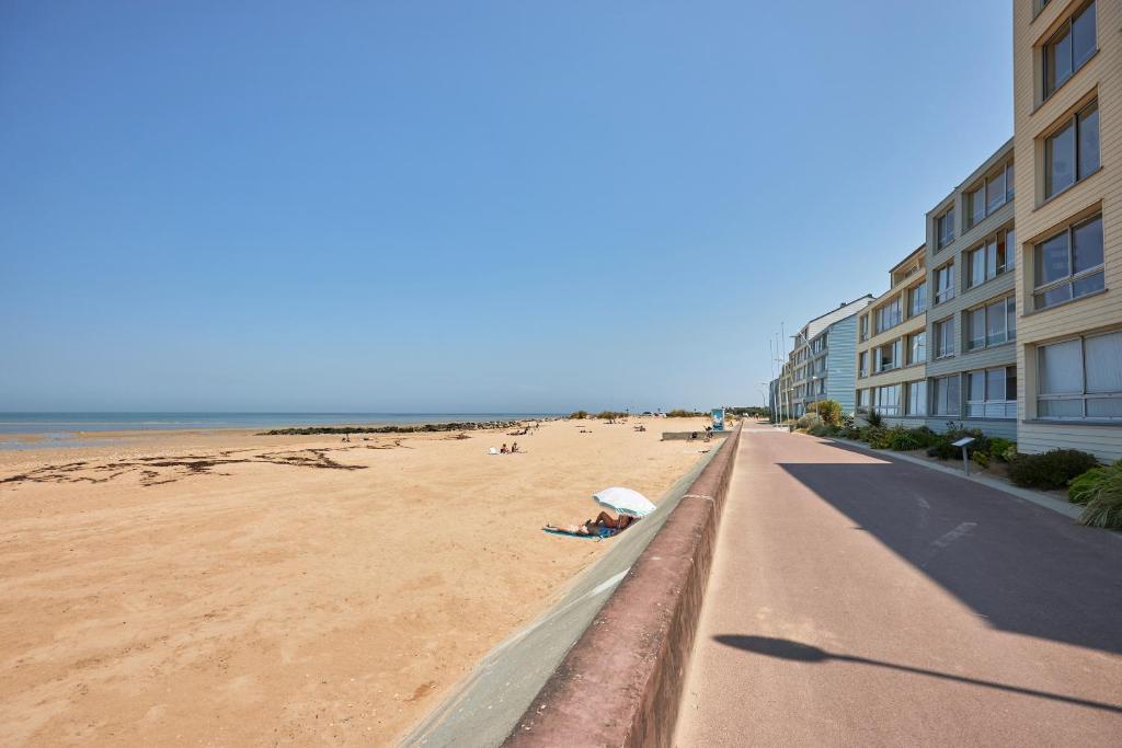 - une plage de sable à côté d'un bâtiment et d'une plage dans l'établissement La Longue Vue - Appt face à la mer, à Courseulles-sur-Mer